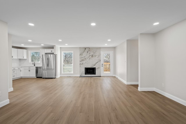 unfurnished living room featuring light hardwood / wood-style flooring, a high end fireplace, a healthy amount of sunlight, and sink