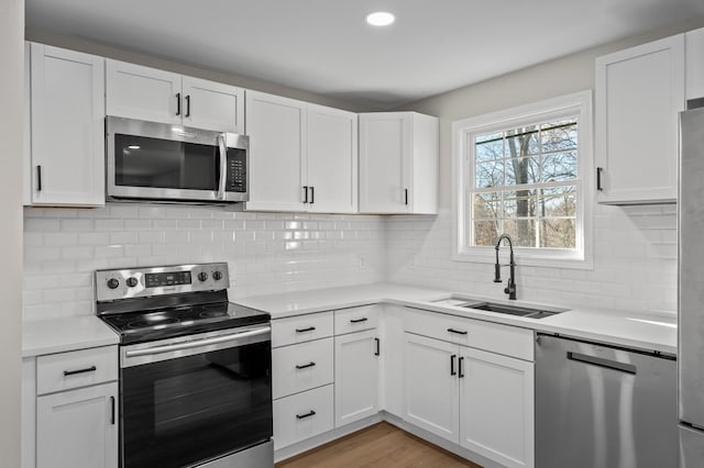 kitchen featuring backsplash, sink, light wood-type flooring, white cabinetry, and stainless steel appliances