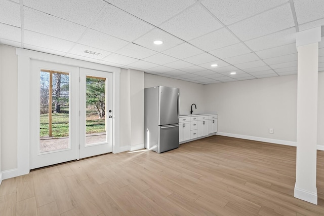 interior space featuring a drop ceiling, light hardwood / wood-style floors, sink, and stainless steel refrigerator