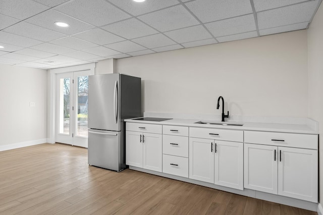 kitchen with white cabinetry, sink, light hardwood / wood-style flooring, stainless steel fridge, and black electric stovetop