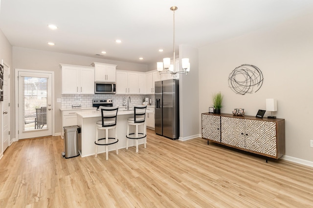 kitchen featuring hanging light fixtures, stainless steel appliances, a kitchen bar, a kitchen island, and white cabinetry