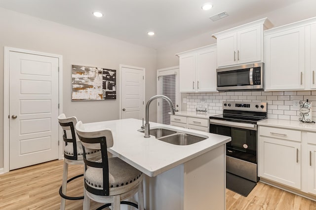 kitchen with stainless steel appliances, a center island with sink, white cabinetry, and sink