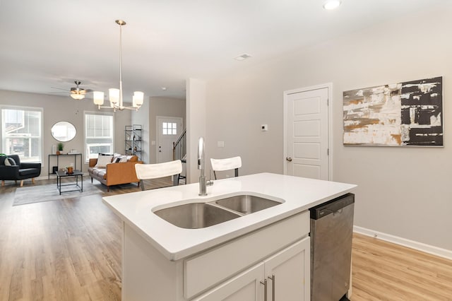 kitchen featuring stainless steel dishwasher, decorative light fixtures, a kitchen island with sink, white cabinets, and sink