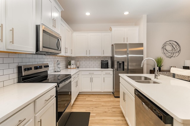 kitchen with stainless steel appliances, white cabinetry, light hardwood / wood-style floors, and sink