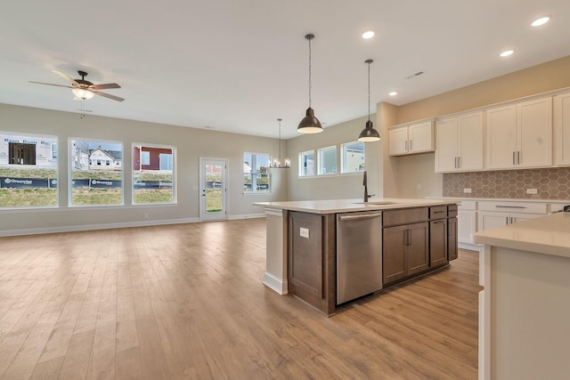 kitchen with tasteful backsplash, white cabinets, decorative light fixtures, dishwasher, and an island with sink