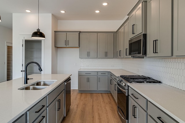 kitchen featuring sink, gray cabinets, light wood-type flooring, appliances with stainless steel finishes, and decorative light fixtures