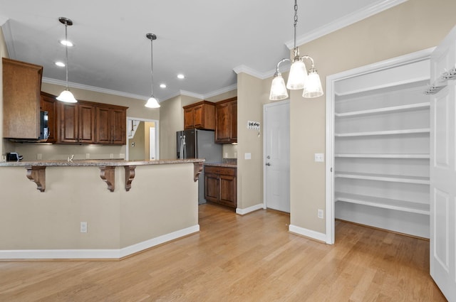 kitchen featuring a breakfast bar area, built in shelves, crown molding, and hanging light fixtures