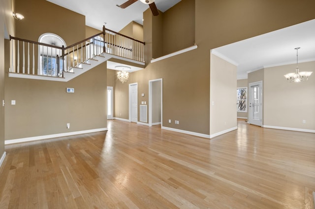 unfurnished living room featuring crown molding, a towering ceiling, ceiling fan with notable chandelier, and light wood-type flooring