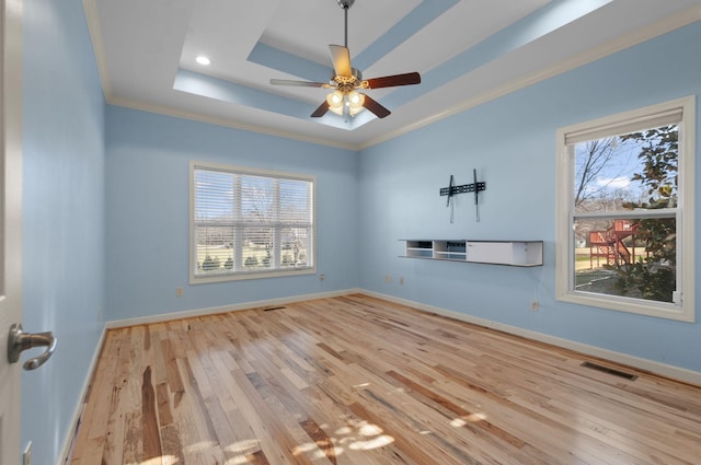 unfurnished room with a raised ceiling, a wealth of natural light, crown molding, and light wood-type flooring