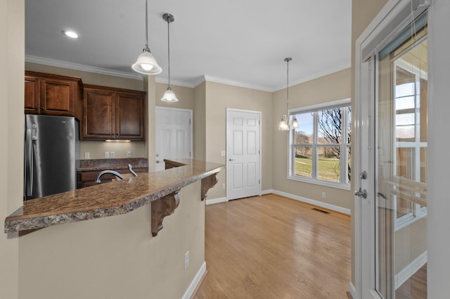 kitchen with decorative light fixtures, ornamental molding, a breakfast bar area, and stainless steel refrigerator