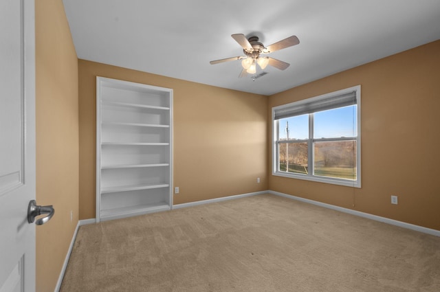 carpeted empty room featuring built in shelves and ceiling fan