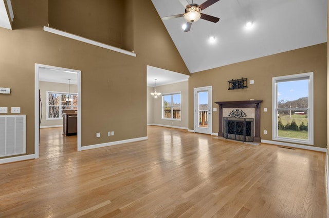 unfurnished living room featuring ceiling fan with notable chandelier, high vaulted ceiling, and plenty of natural light