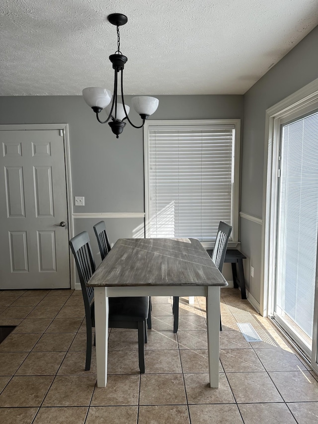 tiled dining space with a textured ceiling and an inviting chandelier