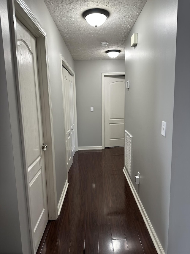 hall with a textured ceiling and dark hardwood / wood-style flooring