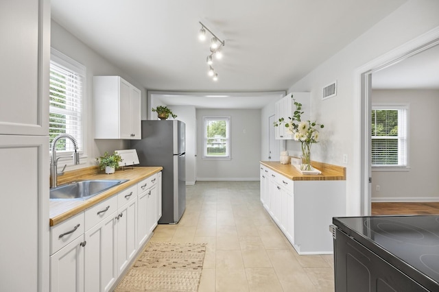 kitchen featuring butcher block counters, range with electric cooktop, sink, stainless steel fridge, and white cabinetry