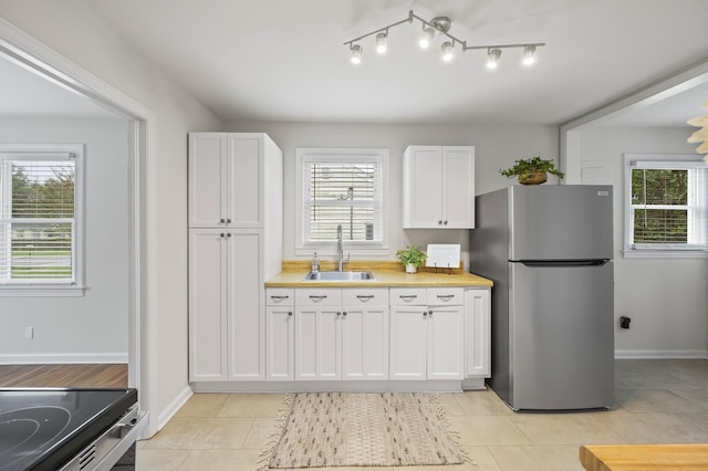 kitchen with stainless steel fridge, light tile patterned floors, white cabinetry, and sink