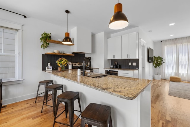 kitchen with kitchen peninsula, white cabinetry, and light stone countertops