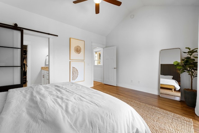 bedroom with ceiling fan, a barn door, ensuite bathroom, light hardwood / wood-style floors, and vaulted ceiling