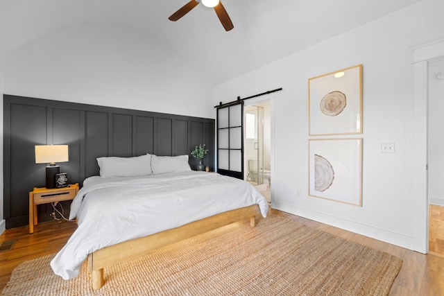 bedroom featuring connected bathroom, ceiling fan, a barn door, light hardwood / wood-style flooring, and vaulted ceiling