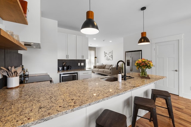 kitchen with sink, hanging light fixtures, built in microwave, white cabinetry, and kitchen peninsula