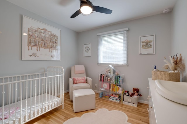 bedroom with hardwood / wood-style floors, ceiling fan, and a nursery area