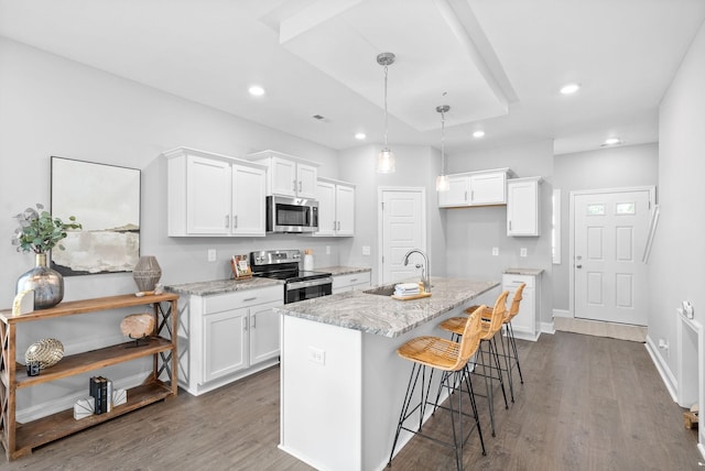 kitchen featuring white cabinets, appliances with stainless steel finishes, a center island with sink, and light stone counters