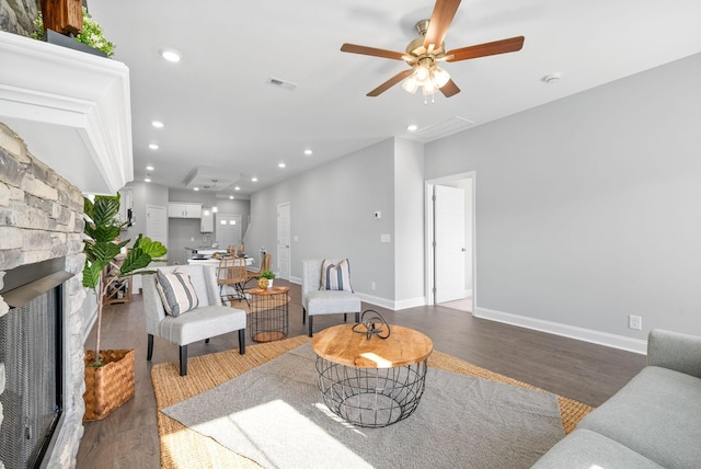 living room with ceiling fan, dark hardwood / wood-style flooring, and a stone fireplace