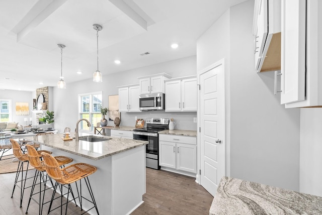 kitchen with light stone countertops, stainless steel appliances, sink, white cabinetry, and hanging light fixtures