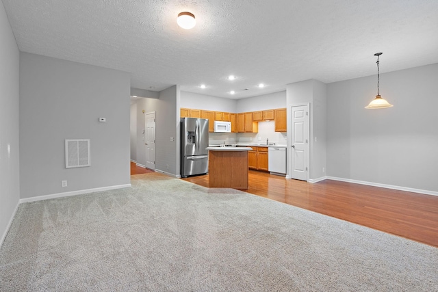 kitchen featuring light colored carpet, a textured ceiling, pendant lighting, white appliances, and a kitchen island