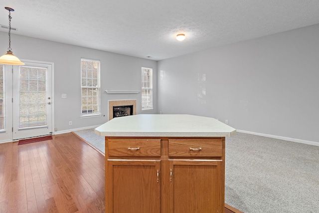 kitchen featuring light wood-type flooring, a textured ceiling, a tile fireplace, pendant lighting, and a kitchen island