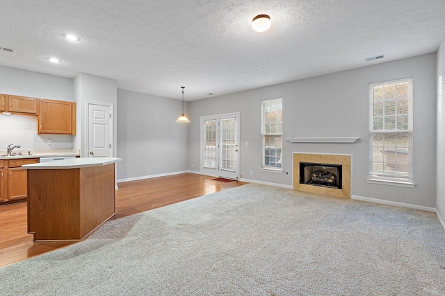 kitchen with a textured ceiling, light colored carpet, sink, pendant lighting, and a tiled fireplace