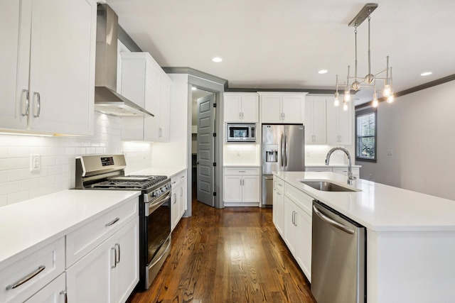 kitchen with white cabinetry, sink, stainless steel appliances, wall chimney range hood, and an island with sink