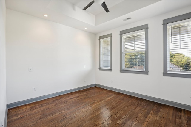 empty room with dark hardwood / wood-style floors, ceiling fan, and a tray ceiling