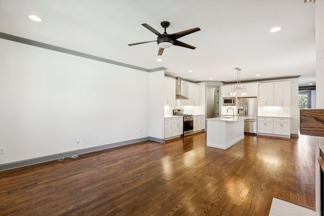 kitchen with wall chimney exhaust hood, stainless steel appliances, decorative light fixtures, a center island with sink, and white cabinets