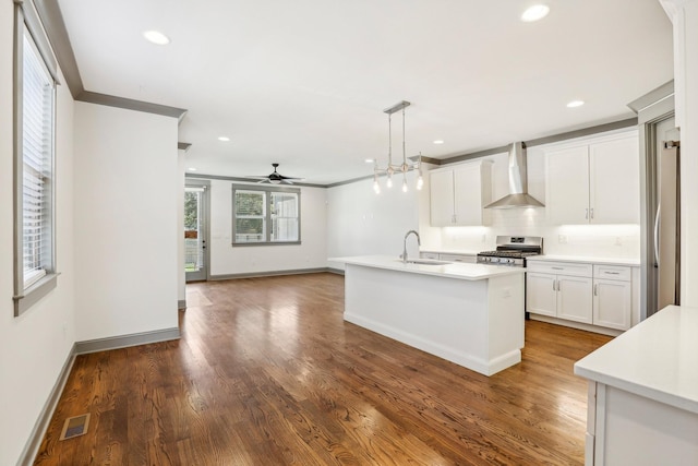 kitchen featuring a center island with sink, white cabinets, hanging light fixtures, wall chimney exhaust hood, and appliances with stainless steel finishes