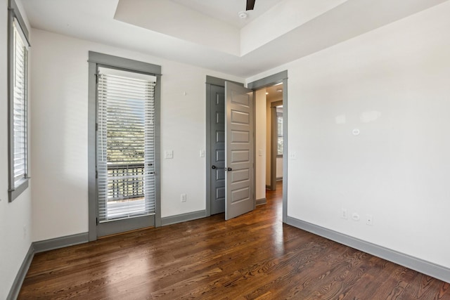 unfurnished bedroom featuring dark hardwood / wood-style flooring, a raised ceiling, and ceiling fan