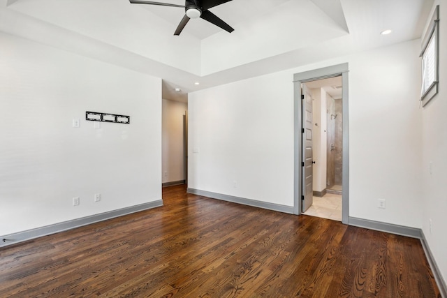 empty room featuring ceiling fan, wood-type flooring, and a tray ceiling