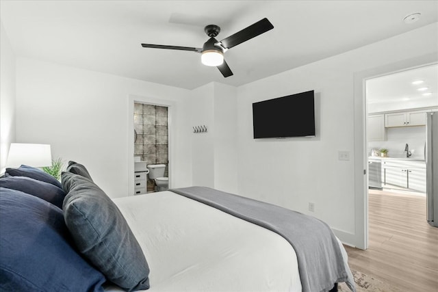 bedroom with stainless steel refrigerator, ceiling fan, sink, ensuite bathroom, and light wood-type flooring