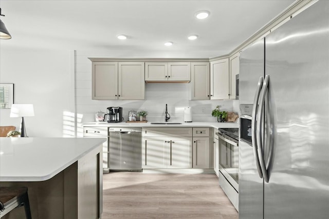 kitchen featuring pendant lighting, sink, decorative backsplash, light hardwood / wood-style floors, and stainless steel appliances