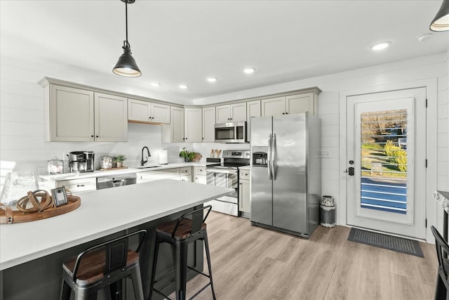 kitchen with appliances with stainless steel finishes, sink, light hardwood / wood-style flooring, hanging light fixtures, and a breakfast bar area