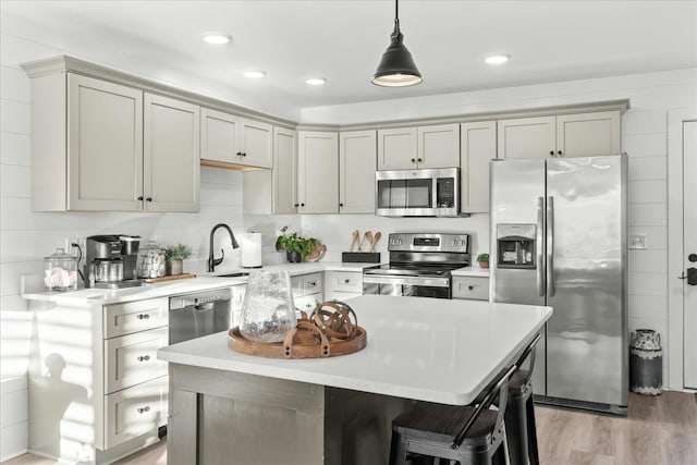 kitchen with hanging light fixtures, sink, light hardwood / wood-style flooring, appliances with stainless steel finishes, and a kitchen island