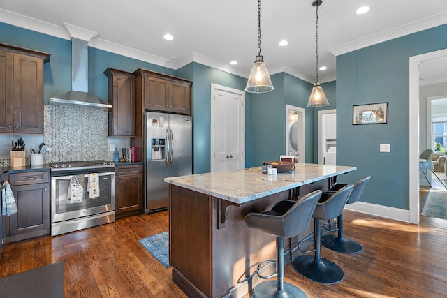 kitchen with wall chimney range hood, backsplash, pendant lighting, a kitchen island, and appliances with stainless steel finishes