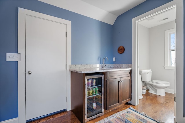 bar featuring sink, beverage cooler, dark hardwood / wood-style flooring, vaulted ceiling, and dark brown cabinets