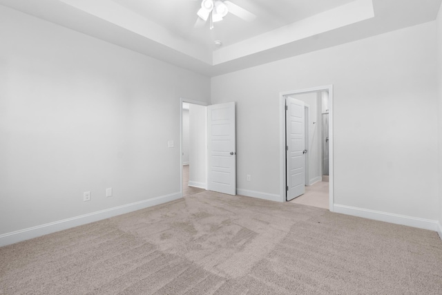 unfurnished bedroom with ceiling fan, a raised ceiling, and light colored carpet