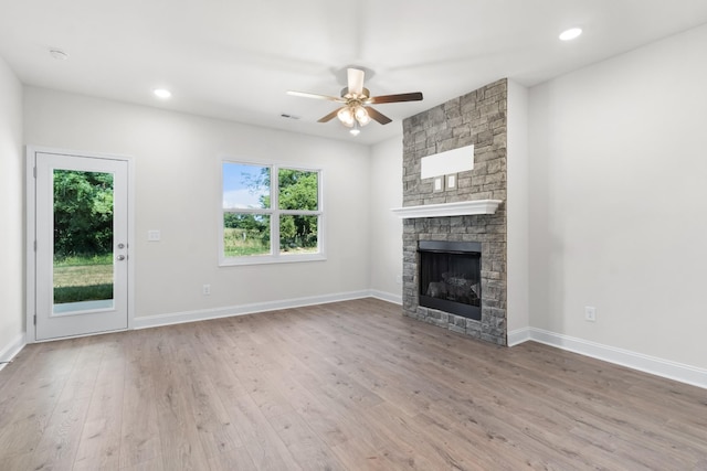 unfurnished living room featuring hardwood / wood-style flooring, ceiling fan, a healthy amount of sunlight, and a stone fireplace