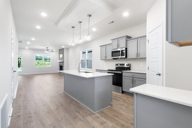 kitchen featuring gray cabinets, ceiling fan, a center island with sink, and stainless steel appliances