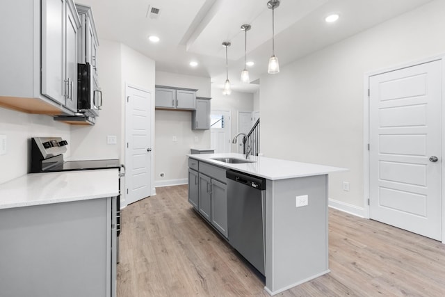 kitchen with appliances with stainless steel finishes, a kitchen island with sink, sink, decorative light fixtures, and light hardwood / wood-style flooring