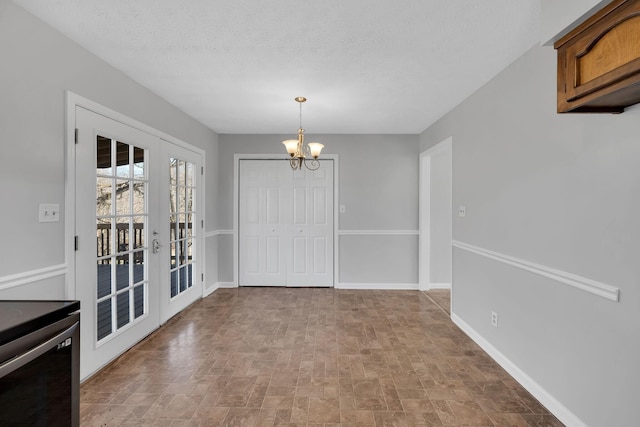 unfurnished dining area with a chandelier, a textured ceiling, and french doors