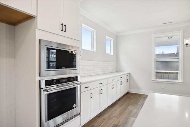 kitchen featuring backsplash, light wood-type flooring, ornamental molding, appliances with stainless steel finishes, and white cabinetry