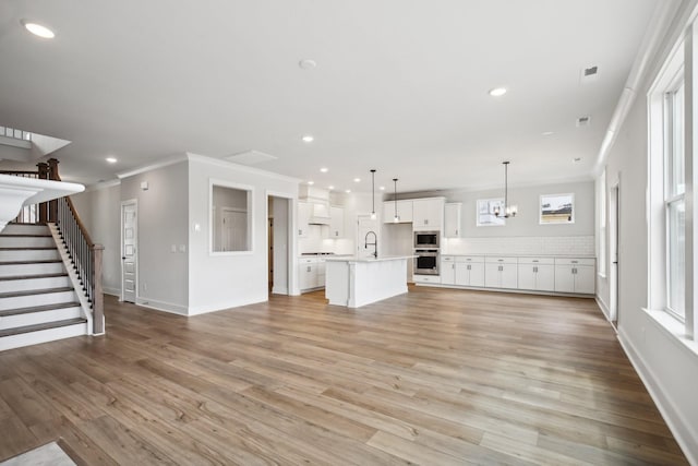 unfurnished living room featuring crown molding, sink, a notable chandelier, and light wood-type flooring